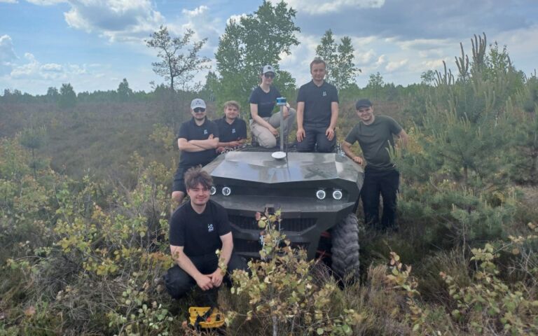 6-ścio osobowa drużyna Łukasiewicz stojąca obok zielonego pojazdu terenowego. Kadr w polu