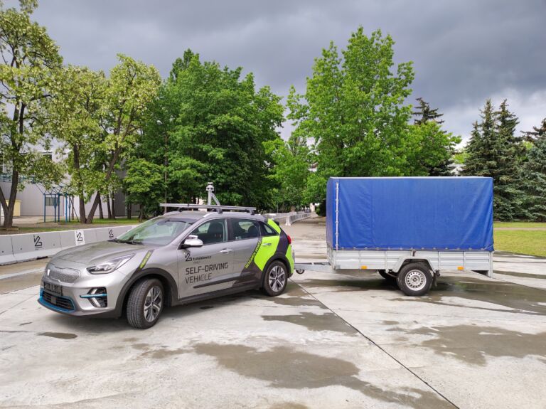 Stojący na betonowym placu szary samochód z logo Łukasiewicz z podpiętą naczepą
